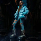 Woman wearing a blue puffer jacket with ripped jeans and winter boots in an urban streetwear setting at night